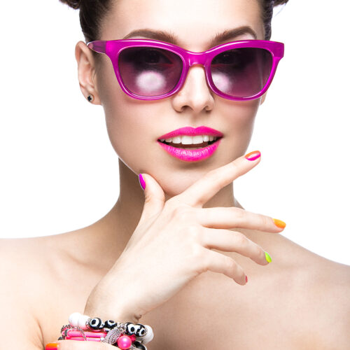 Beautiful girl in pink sunglasses with bright makeup and colorful nails. Beauty face. Picture taken in the studio on a white background.