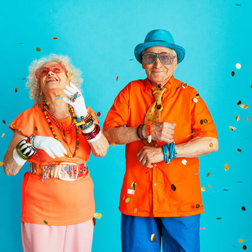 Beautiful senior old couple wearing fancy party clothes acting in studio on a colored background. Conceptual image about third age and seniority, old people feeling young inside.