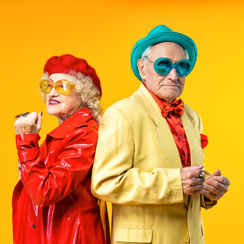 Beautiful senior old couple wearing fancy party clothes acting in studio on a colored background. Conceptual image about third age and seniority, old people feeling young inside.