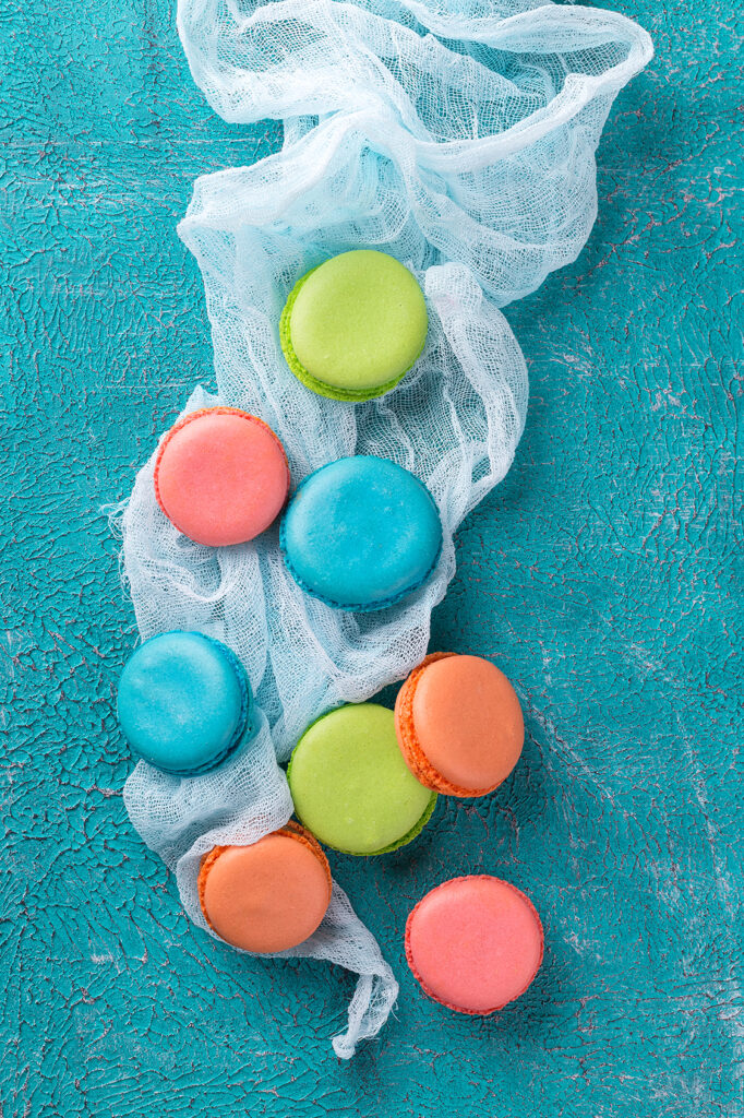 Cake macaron or macaroon on turquoise background from above, colorful almond cookies, pastel colors, vintage card, top view