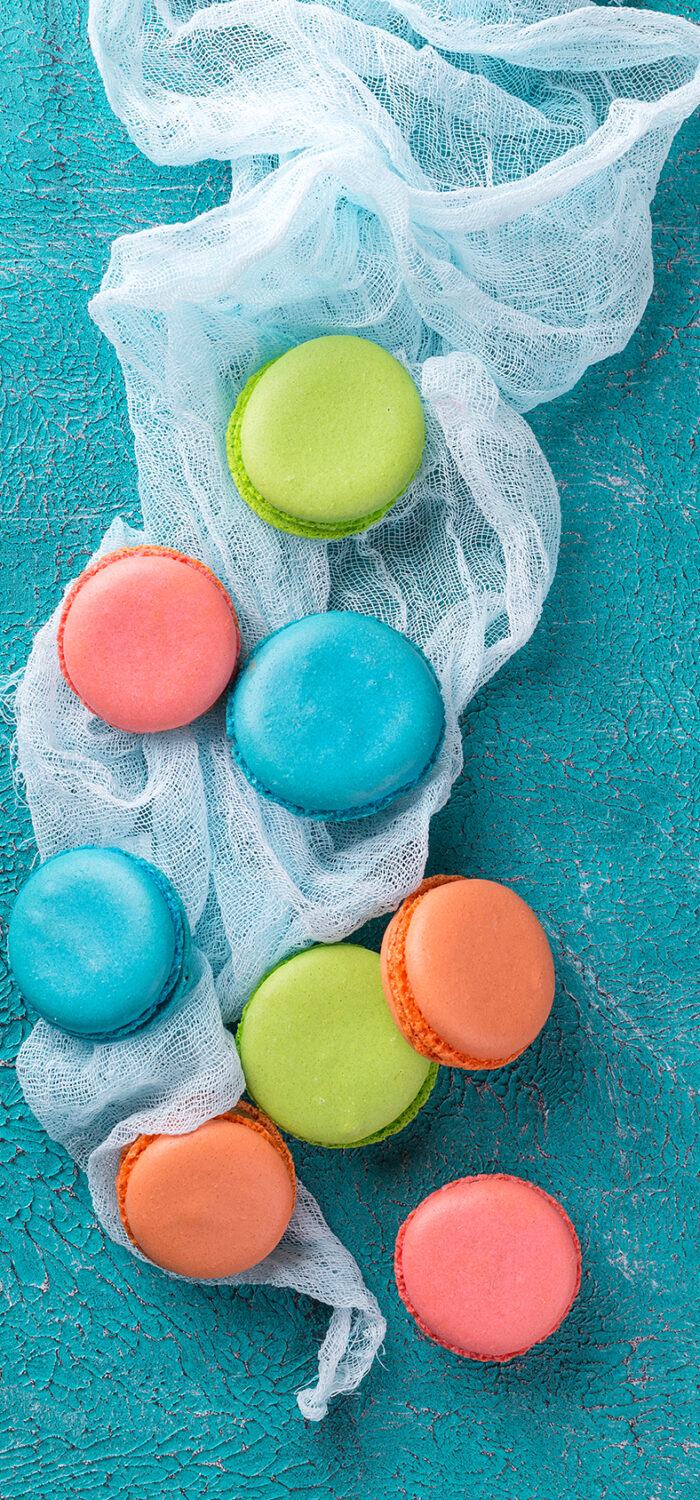 Cake macaron or macaroon on turquoise background from above, colorful almond cookies, pastel colors, vintage card, top view