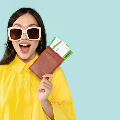 Vacation, travelling. Emotional young lady tourist wearing yellow shirt and sunglasses showing passport and flight tickets boarding pass, grimacing, blue studio background, panorama with copy space
