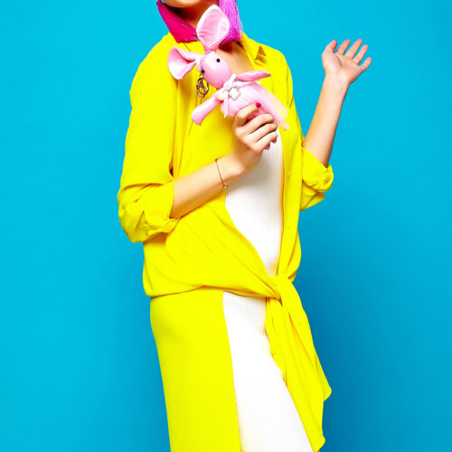 portrait of cheerful fashion hipster girl in casual colorful vivid hipster yellow summer clothes with toy in hands on blue background