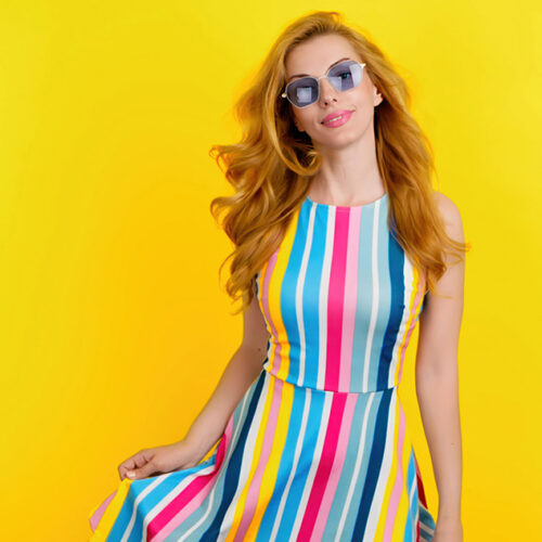 Fashionable redhead woman with smiling face for confidence, positivity, beauty, advert. Relaxed lady posing looking at camera, pride emotion, trendy makeup, vivid outfit in studio on yellow background
