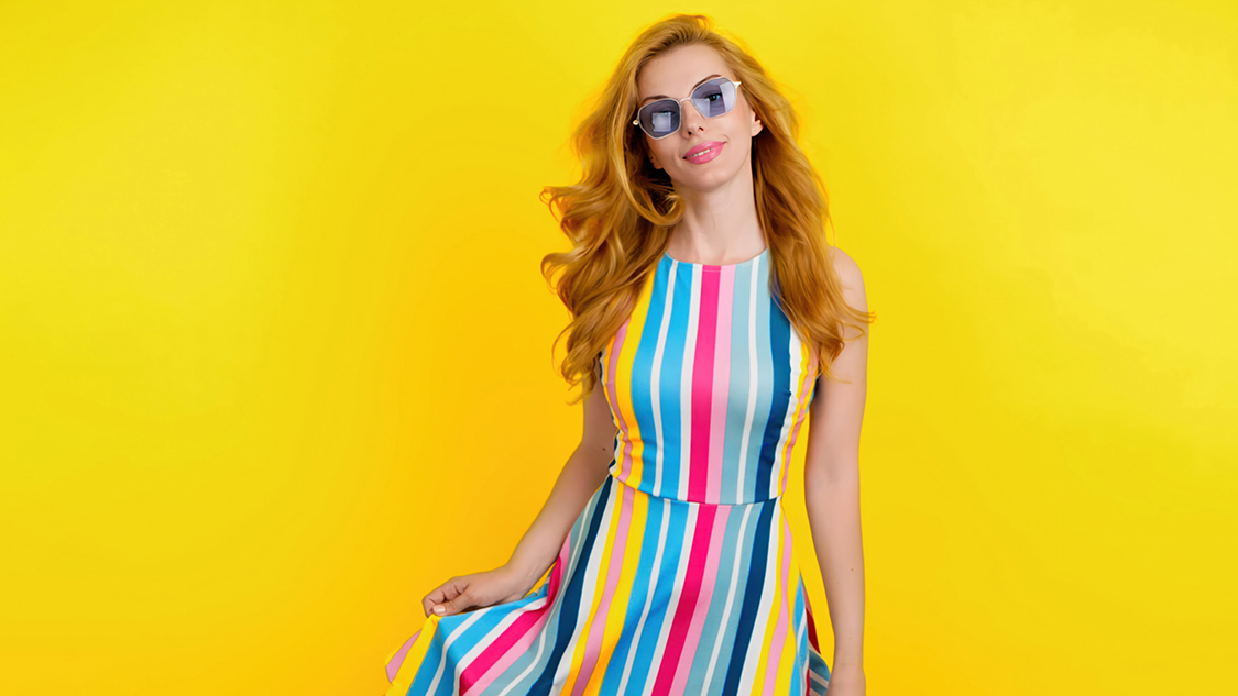 Fashionable redhead woman with smiling face for confidence, positivity, beauty, advert. Relaxed lady posing looking at camera, pride emotion, trendy makeup, vivid outfit in studio on yellow background