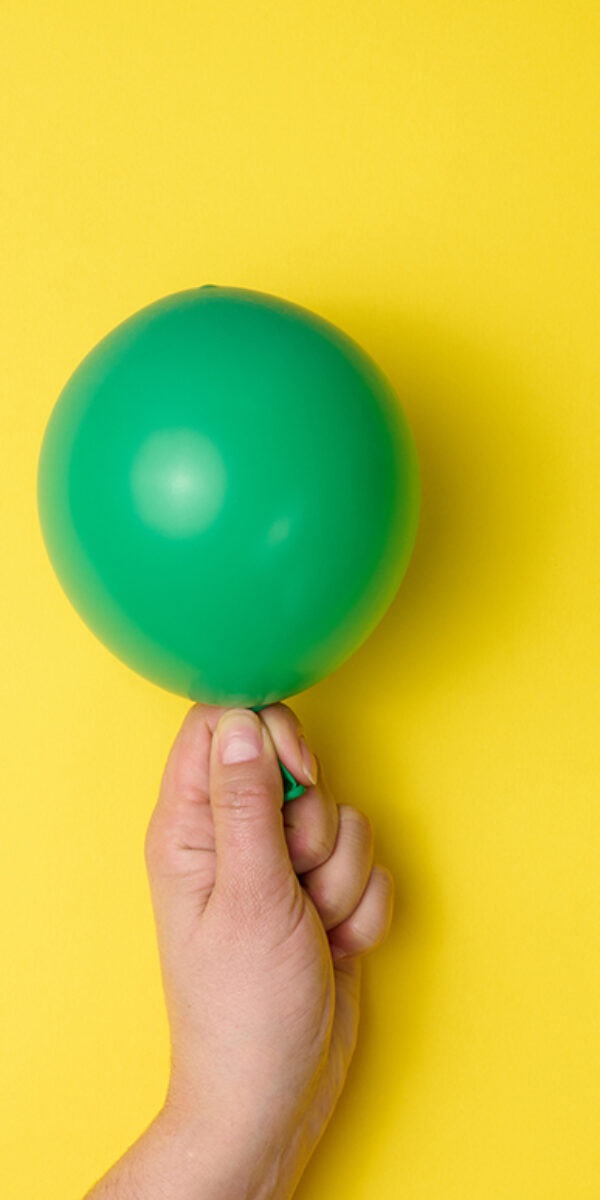 female hand holding an inflated green air balloon on a yellow ba female hand holding an inflated green air balloon on a yellow background, close up