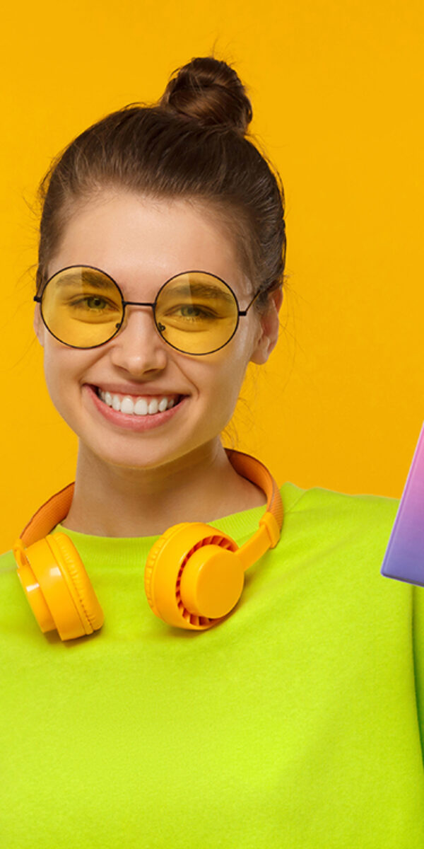 Happy smiling female holding passport with airplane tickets Happy smiling female wearing neon green top, glasses and wireless headphones around neck, holding passport with airplane tickets, isolated on yellow background