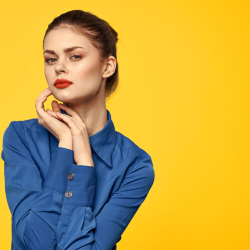 Portrait of a woman in a blue shirt with bright makeup red lips yellow background cropped view. High quality photo