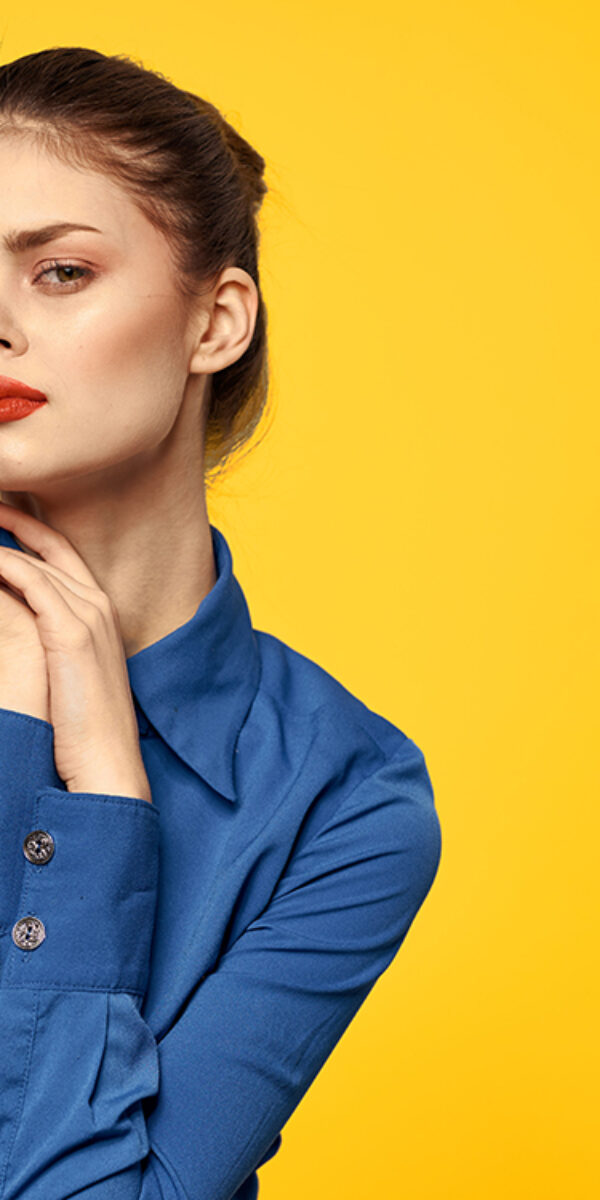 Portrait of a woman in a blue shirt with bright makeup red lips yellow background cropped view. High quality photo