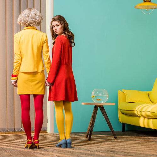 rear view of women in bright retro styled clothing holding hands at colorful apartment, doll house