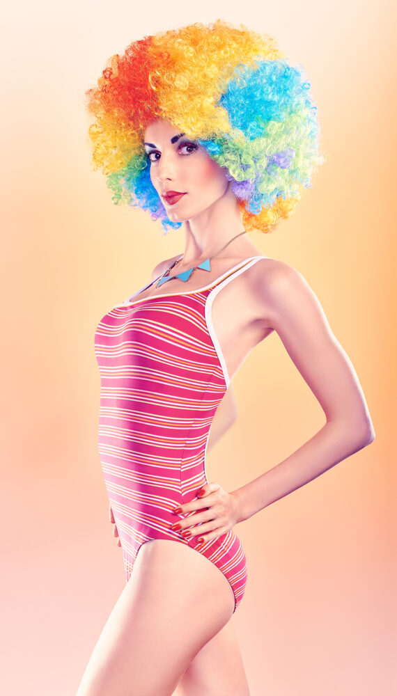 Fashion sexy beauty model slim woman in swimsuit sensually looks, vivid unusual creative people. Provocative attractive girl with trendy necklace on peach, toned. Multicolored afro hairstyle, makeup