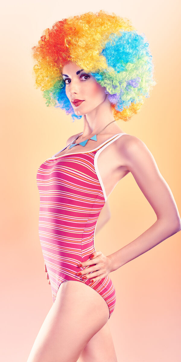 Fashion sexy beauty model slim woman in swimsuit sensually looks, vivid unusual creative people. Provocative attractive girl with trendy necklace on peach, toned. Multicolored afro hairstyle, makeup