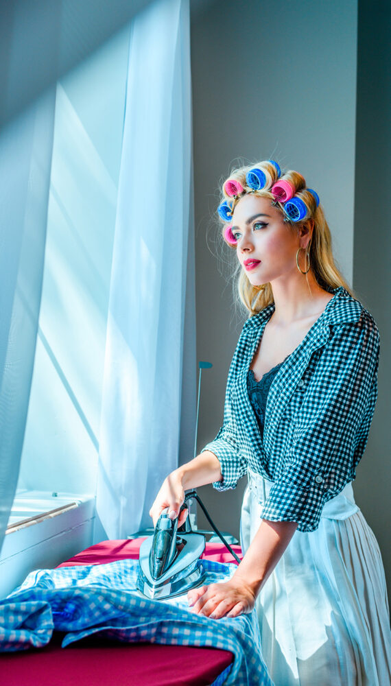 thoughtful beautiful blonde housewife in curlers ironing laundry