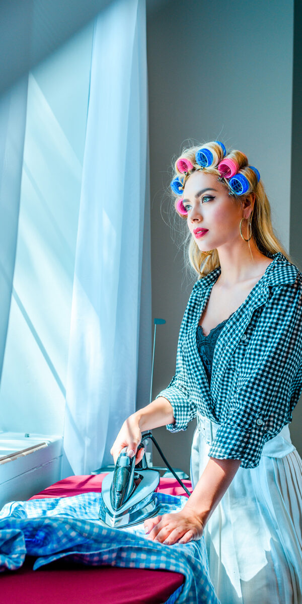 thoughtful beautiful blonde housewife in curlers ironing laundry