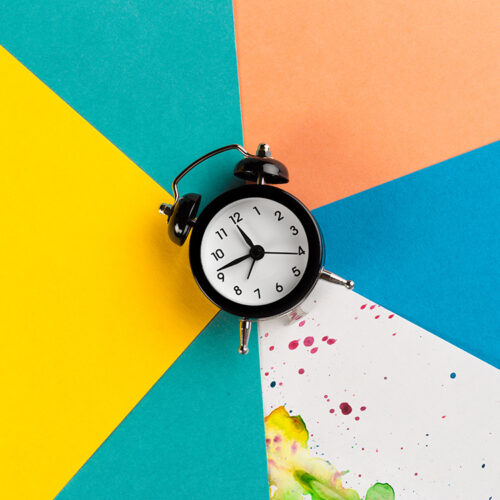 Vintage alarm clock on a creative colorful background with paint sprinkles. Close up.