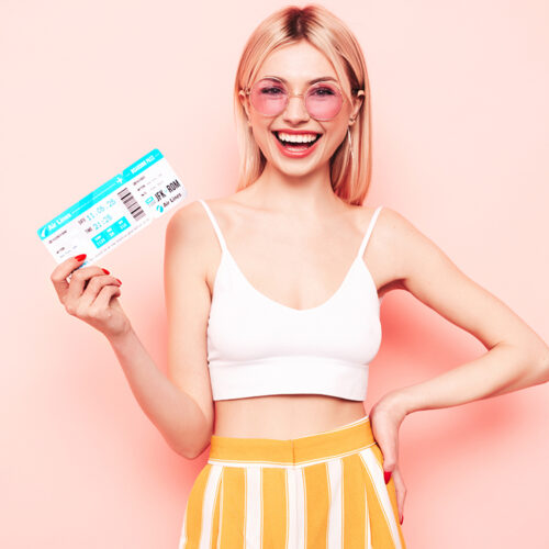 Young beautiful smiling blond female. Carefree woman isolated on pink background. Positive model hold boarding pass ticket. Excited tourist. Passenger travel abroad weekend getaway air flight journey